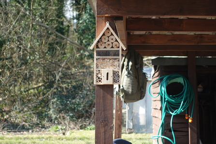 A bug hotel mounted on the wall of a shed outside