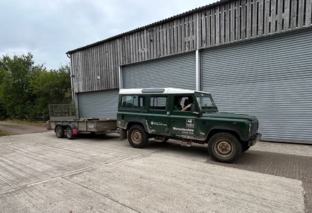 A green Land Rover with a trailer attached; parked outside a barn with metal doors