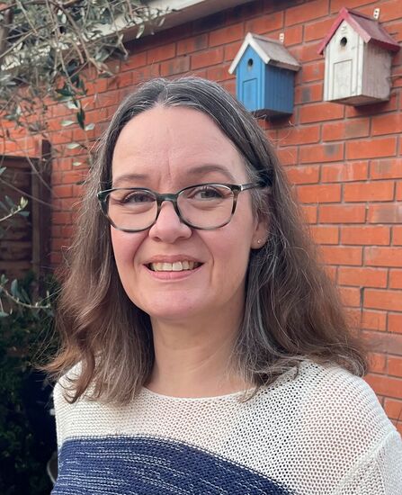 Woman with long dark hair and glasses looking at the camera and smiling