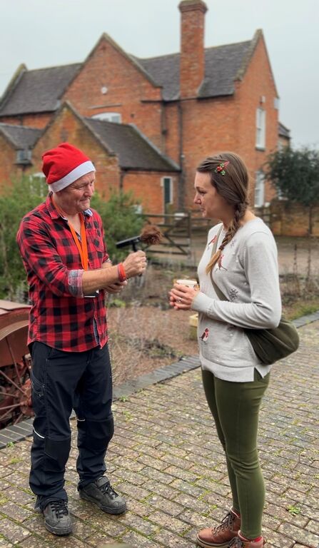 Photograph of a podcast host wearing a Father Christmas hat holding a microphone interviewing a member of staff in a courtyard