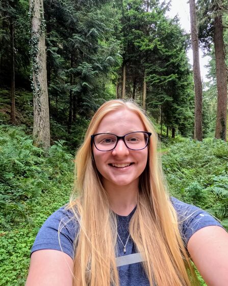 A selfie of Ellie Watton standing in a woodland. She is wearing glasses and has long blonde hair