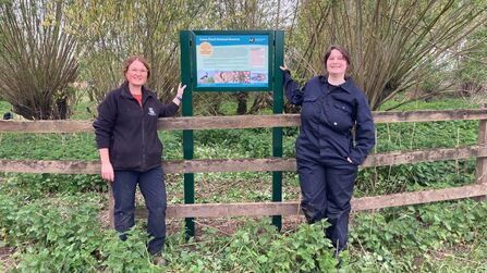A photo of two trainees standing either side of a new interpretation panel at a nature reserve