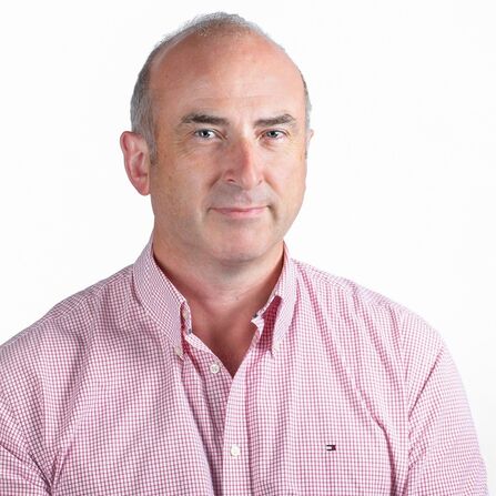 A headshot photo of staff member Richard wearing a pink checked shirt. 
