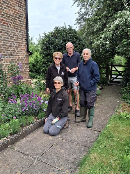 A photo of four garden volunteers standing in front of the flower border at Lower Smite Farm on a path with a gate behind them