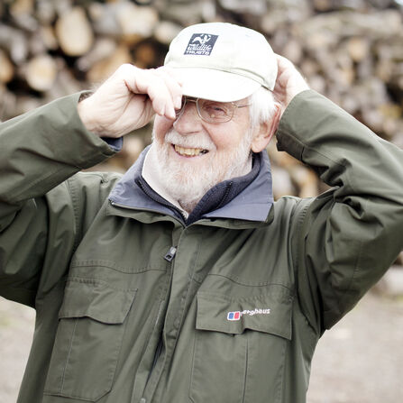  Man with grey hair and a beard is laughing at the camera as he pulls on a baseball cap with Worcestershire Wildlife Trust's logo