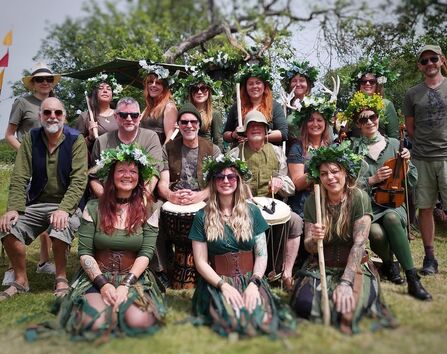 A photo showing a group of Morris dancers in green and brown clothing with leaf crowns kneeling and standing in a group smiling at the camera 