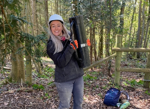 Young woman holding a fence post rammer in a woodland