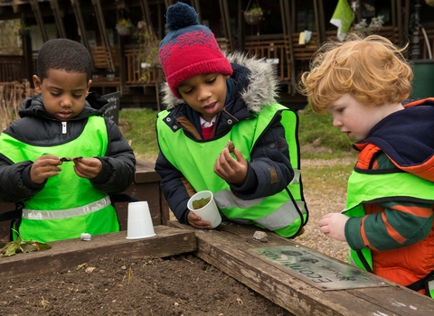 Three children looking at something they've found in the soil by Penny Dixie