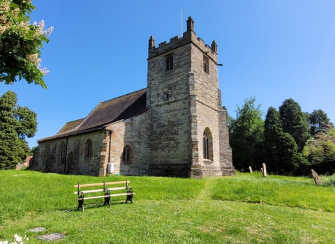 Friends of Feckenham Church surrounded by its grounds. There is a bench visible to the left.