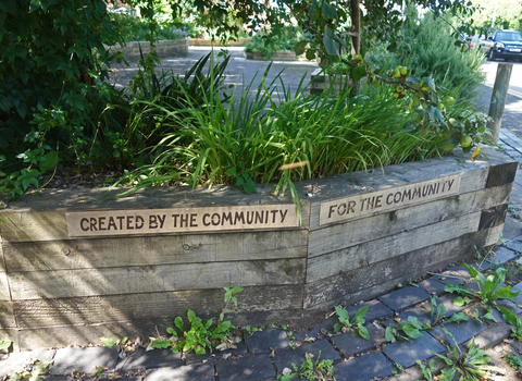 Photo showing a raised bed with plants in and the words 'created by the community for the community' around the bed (by Liz Yorke)