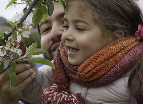 Man lifting a girl to smell blossom on a tree by The Wildlife Trusts