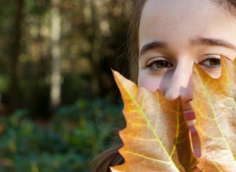 Girl with large autumn leaf in front of face by Tom Marshall