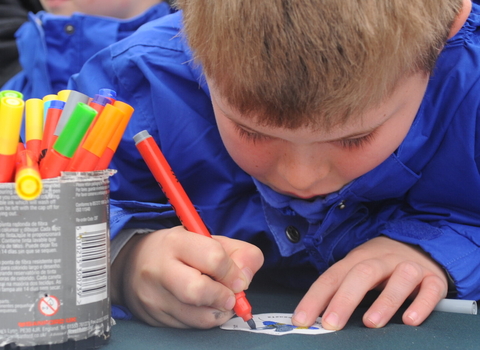 A child colouring in with a tin of coloured pens next to him by Amy Lewis