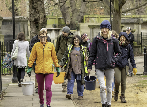 A group of smiling people carrying buckets and walking down a street