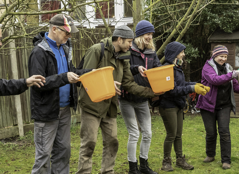 A group of people passing buckets along a line (by Penny Dixie)